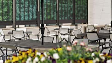 An outdoor seating area with tables and chairs, surrounded by a garden with various flowers.