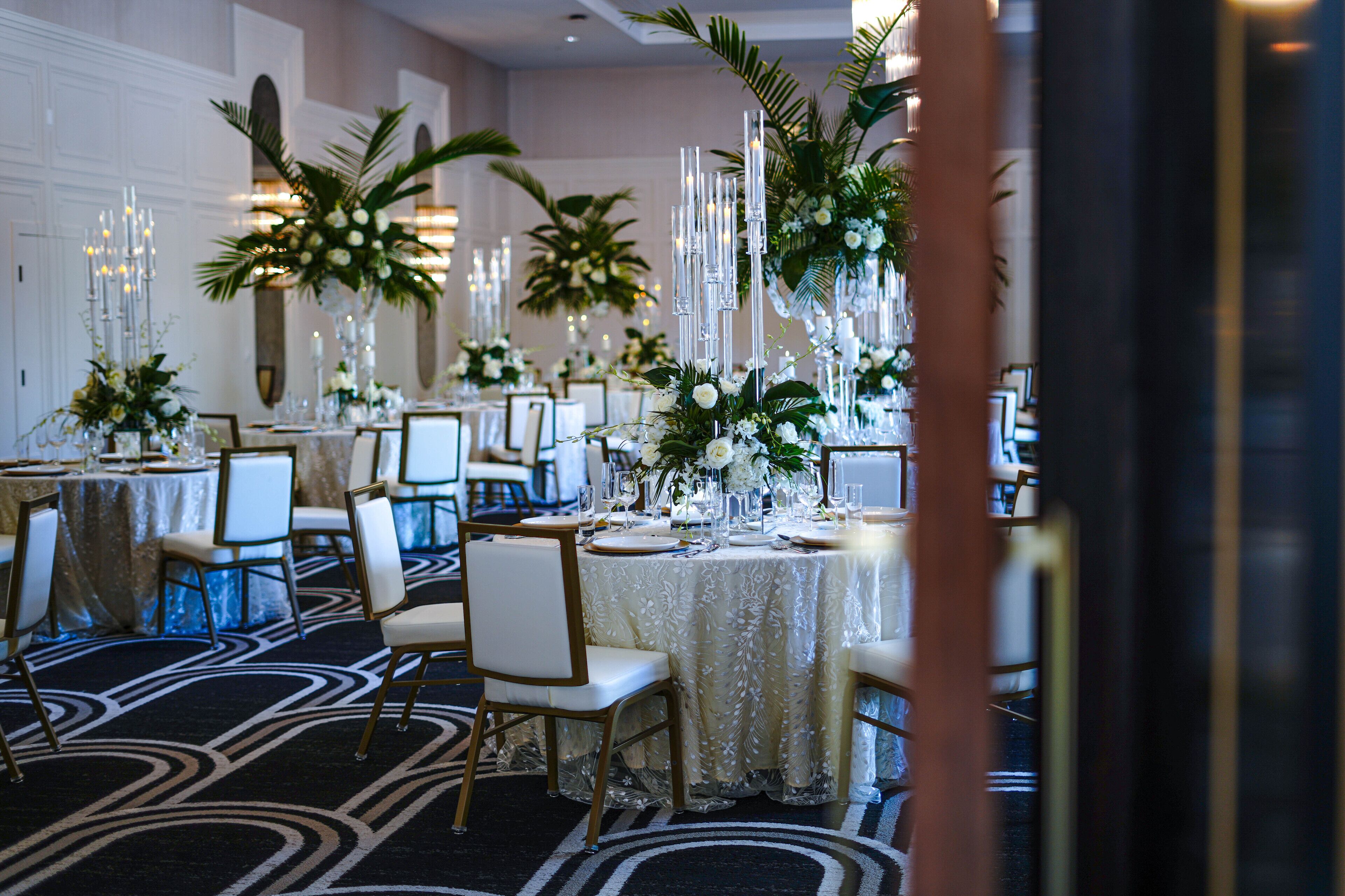 A banquet hall with round tables, white chairs, and floral centerpieces.