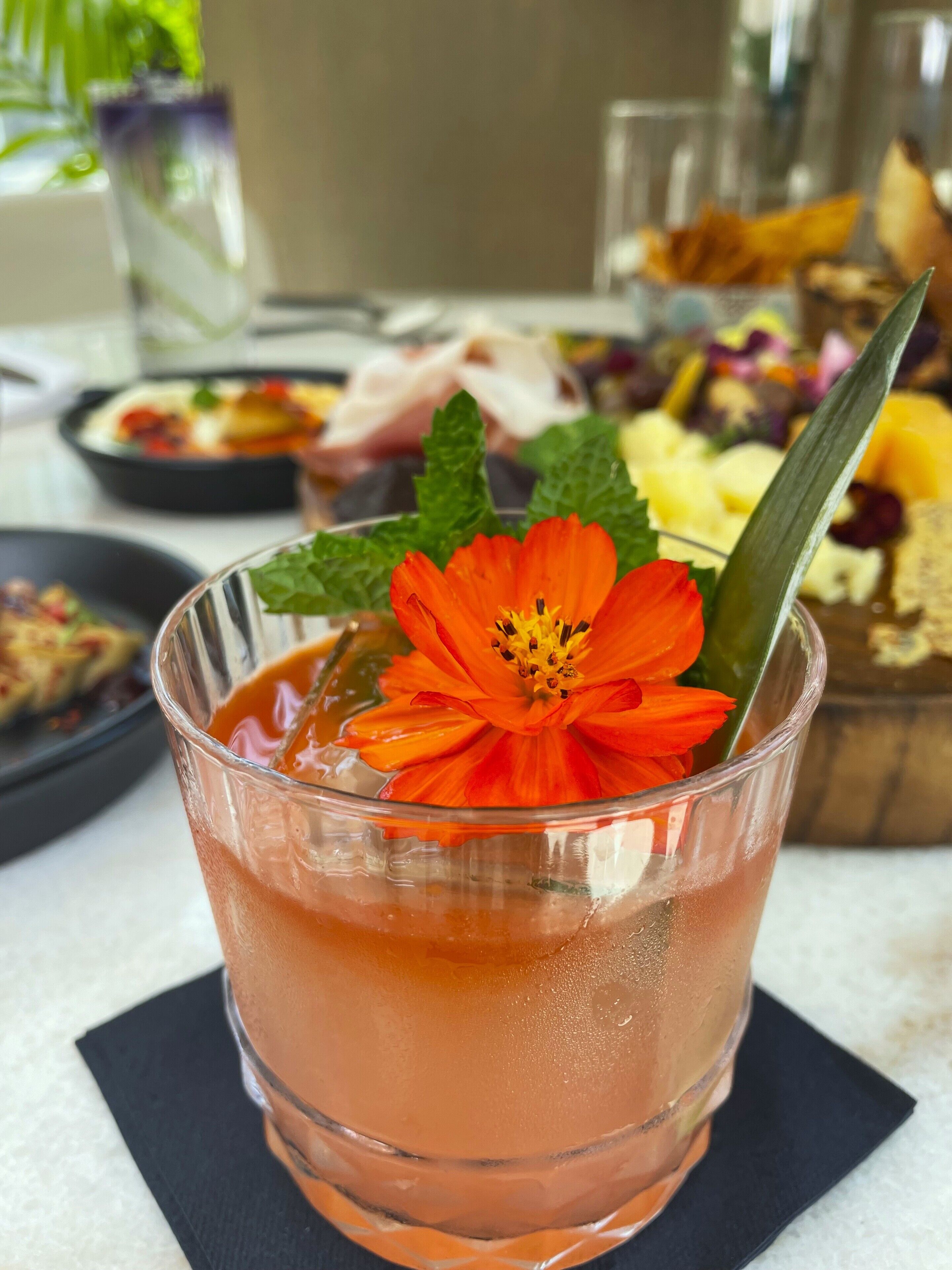A glass of pink beverage with a flower garnish, placed on a black napkin.