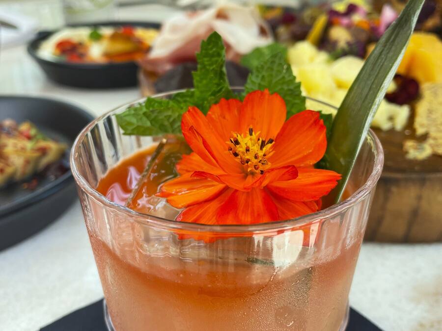 A glass of pink beverage with a flower garnish, placed on a black napkin.