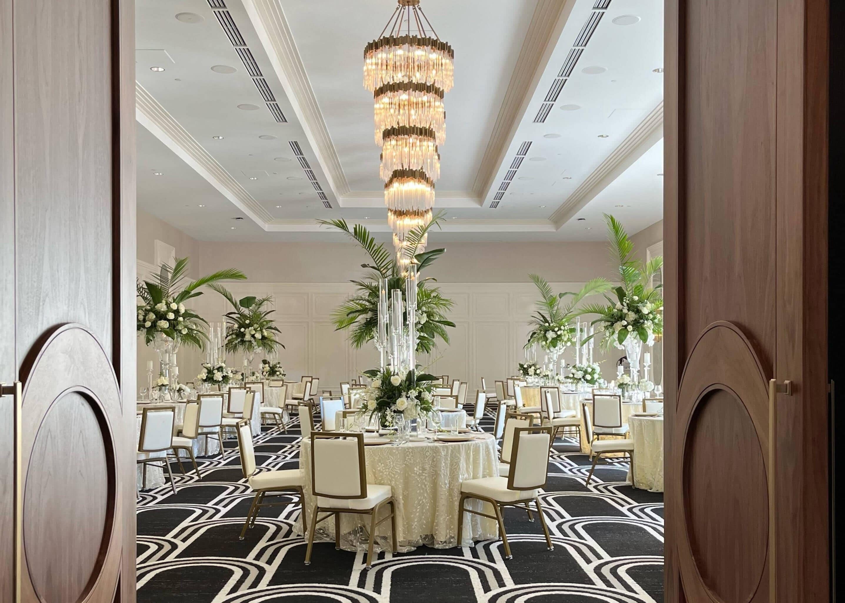 A formal dining room with round tables, elegant chairs, and a large chandelier.