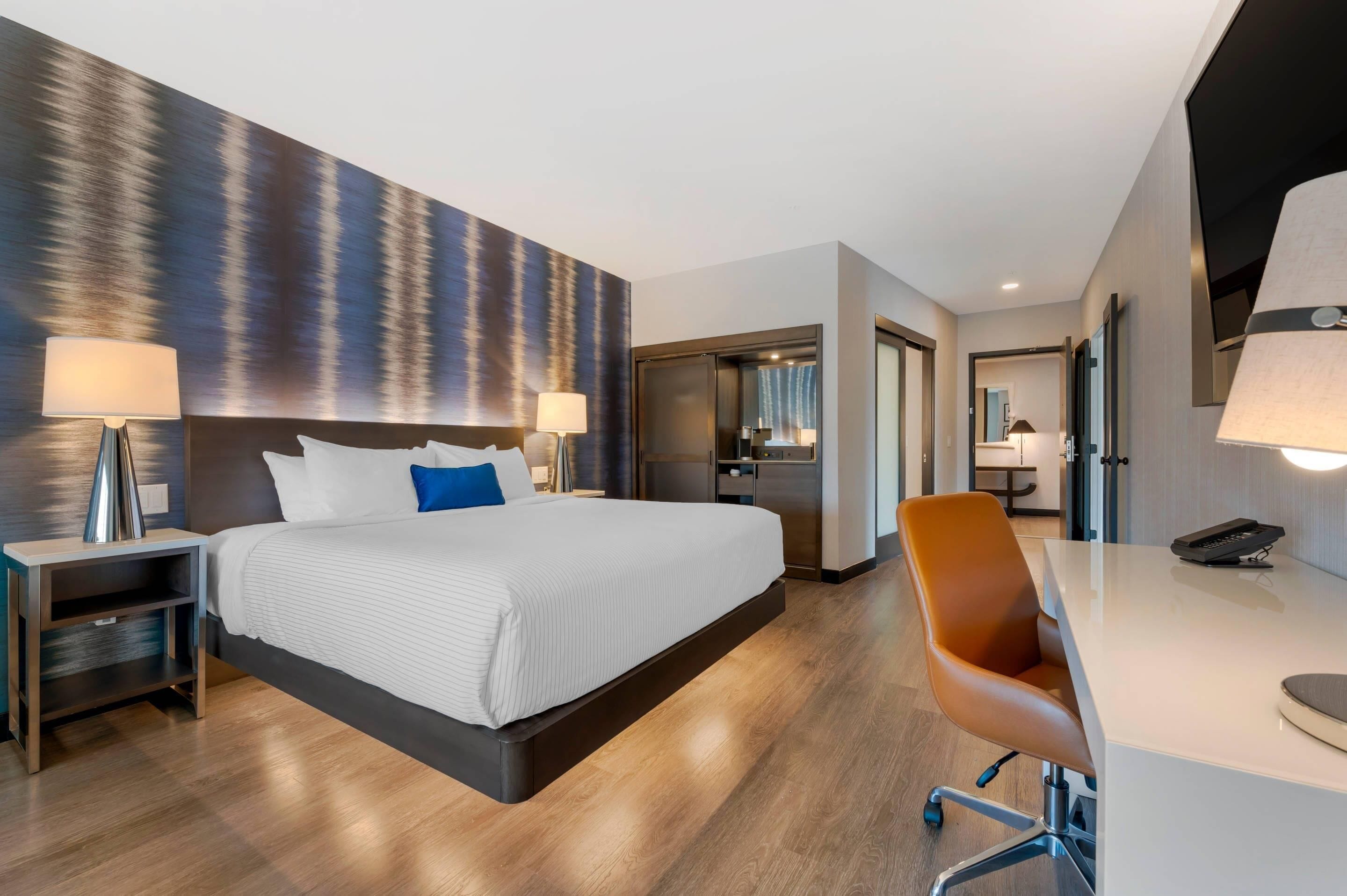 Una habitación de hotel moderna con una cama grande, mesitas de noche, un escritorio y una silla.