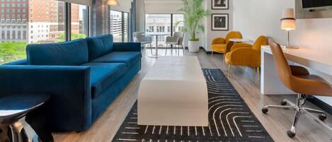 Una sala de estar moderna con un sofá azul, un comedor con sillas amarillas y un amplio ventanal con vistas a la ciudad.