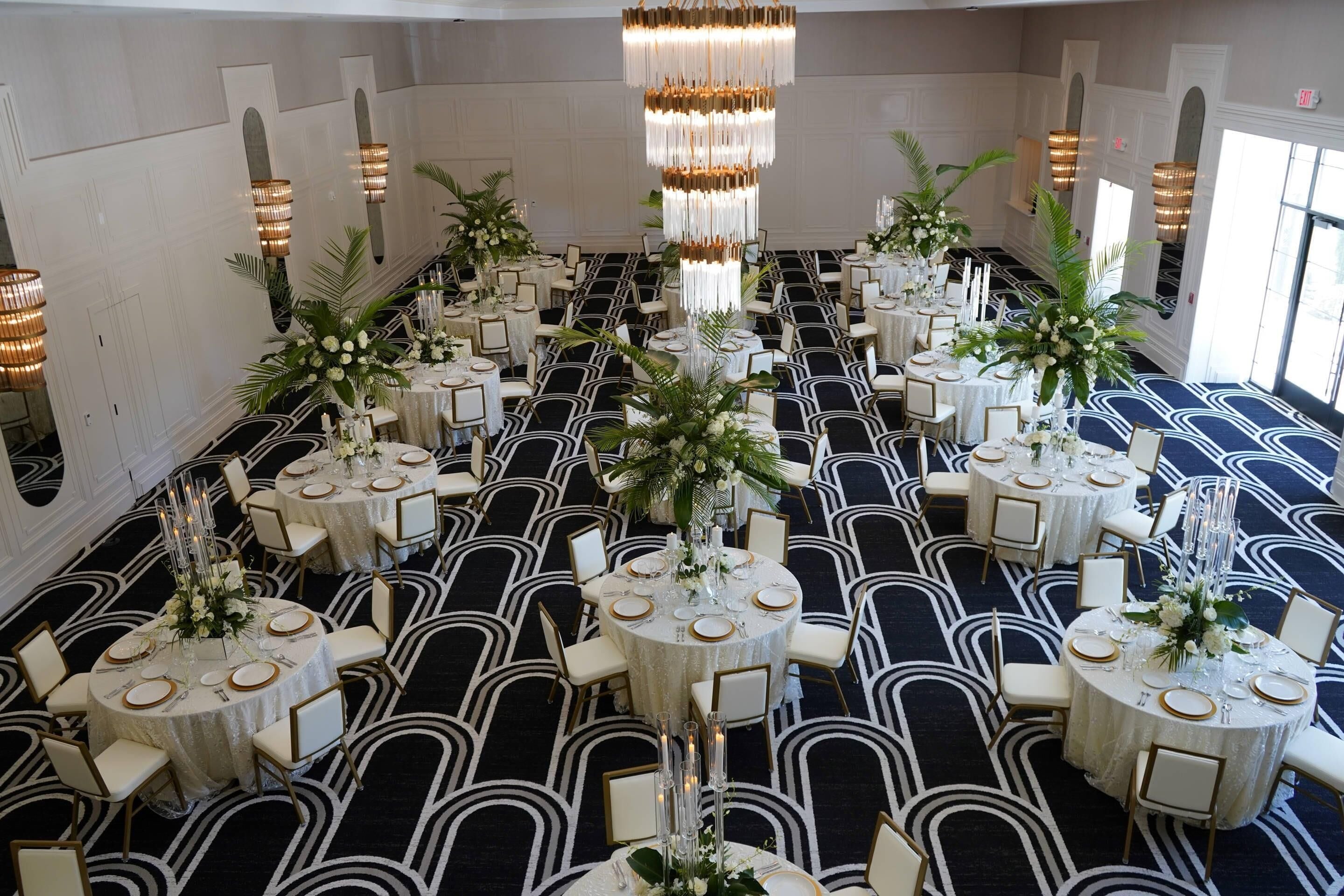 Ein Festsaal mit runden Tischen, weißen Tischdecken und hohen Blumenarrangements.