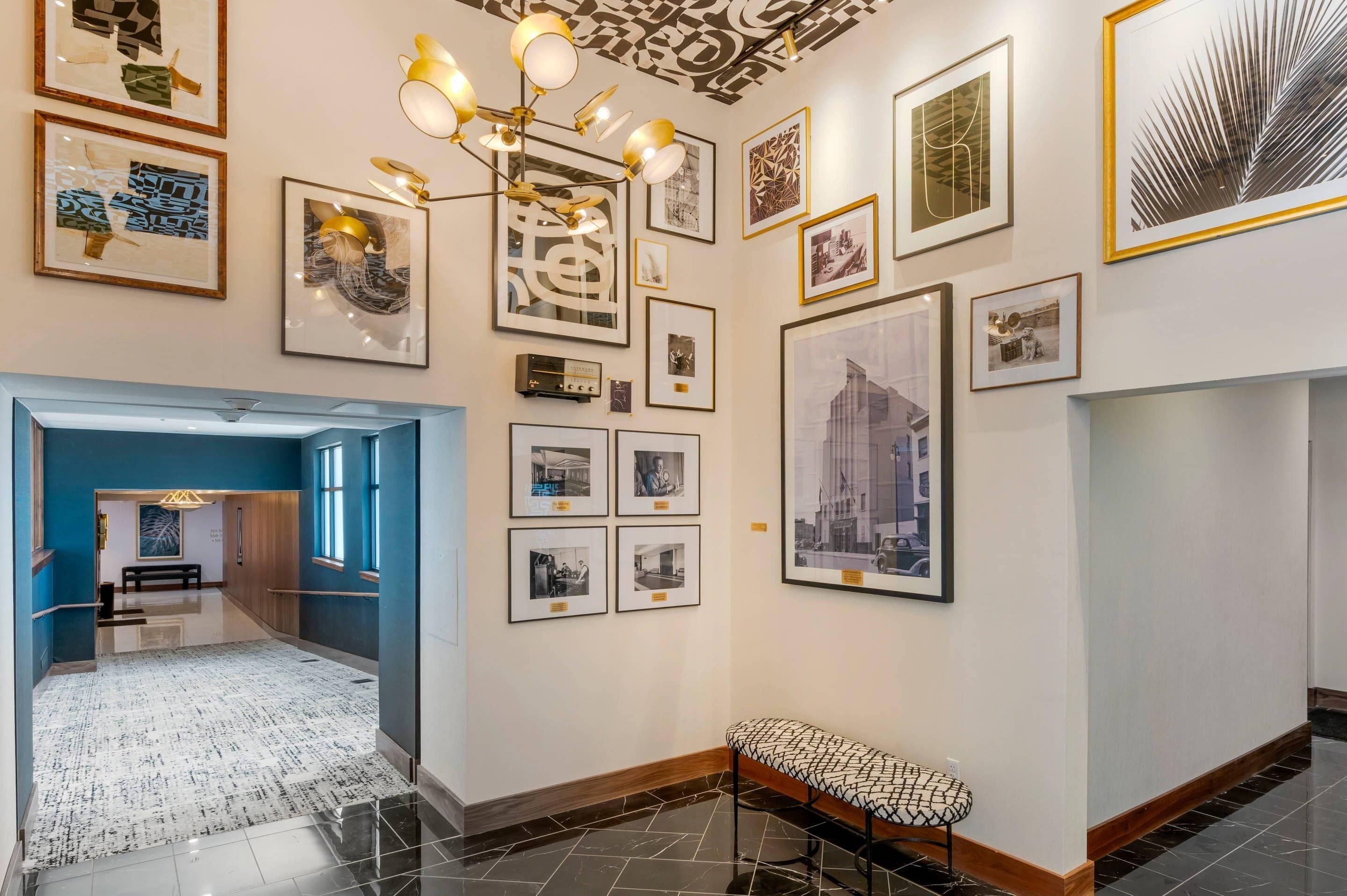 A hallway with framed photographs on the walls, a bench, and a staircase leading to another room.