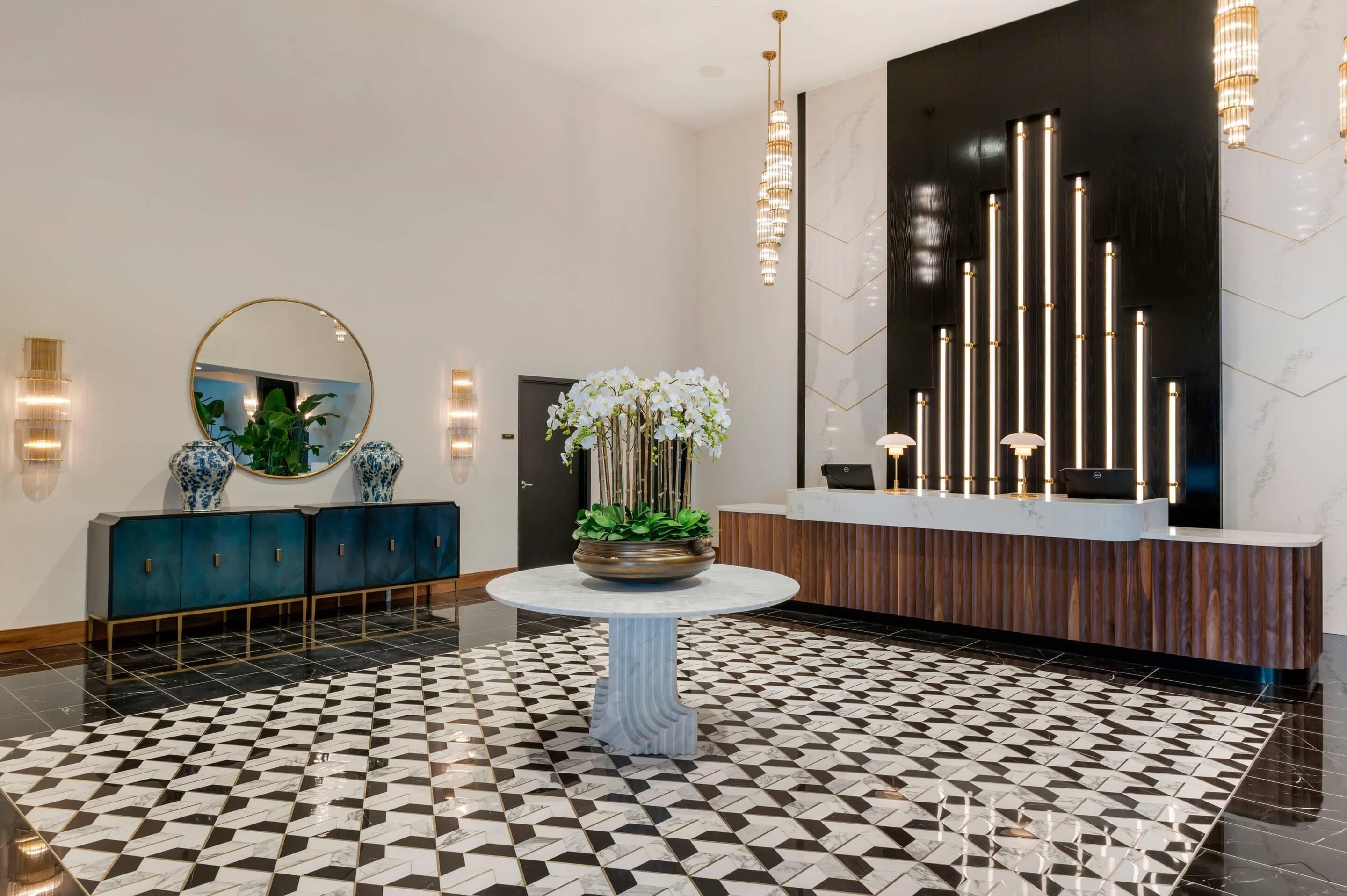 Un hall d’entrée avec un comptoir d’enregistrement, une table ronde ornée d’une plante en pot, un miroir décoratif et un sol à motifs.