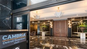 Un vestíbulo con piso de mármol, un mostrador de recepción y un cartel para CAMBRIA Detroit Downtown Valet.