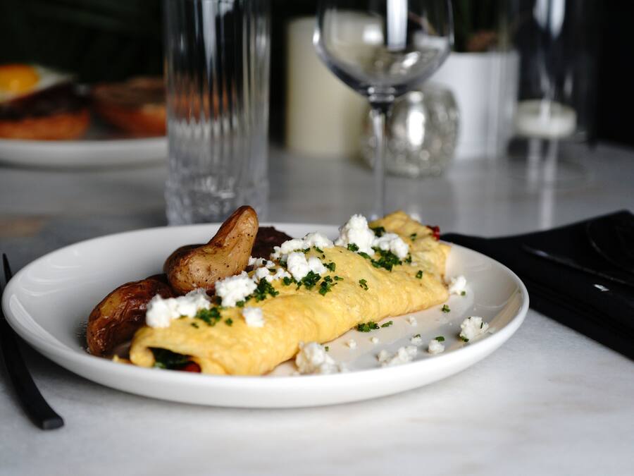 Une assiette de nourriture contenant une omelette, des pommes de terre et du fromage, posée sur une table.