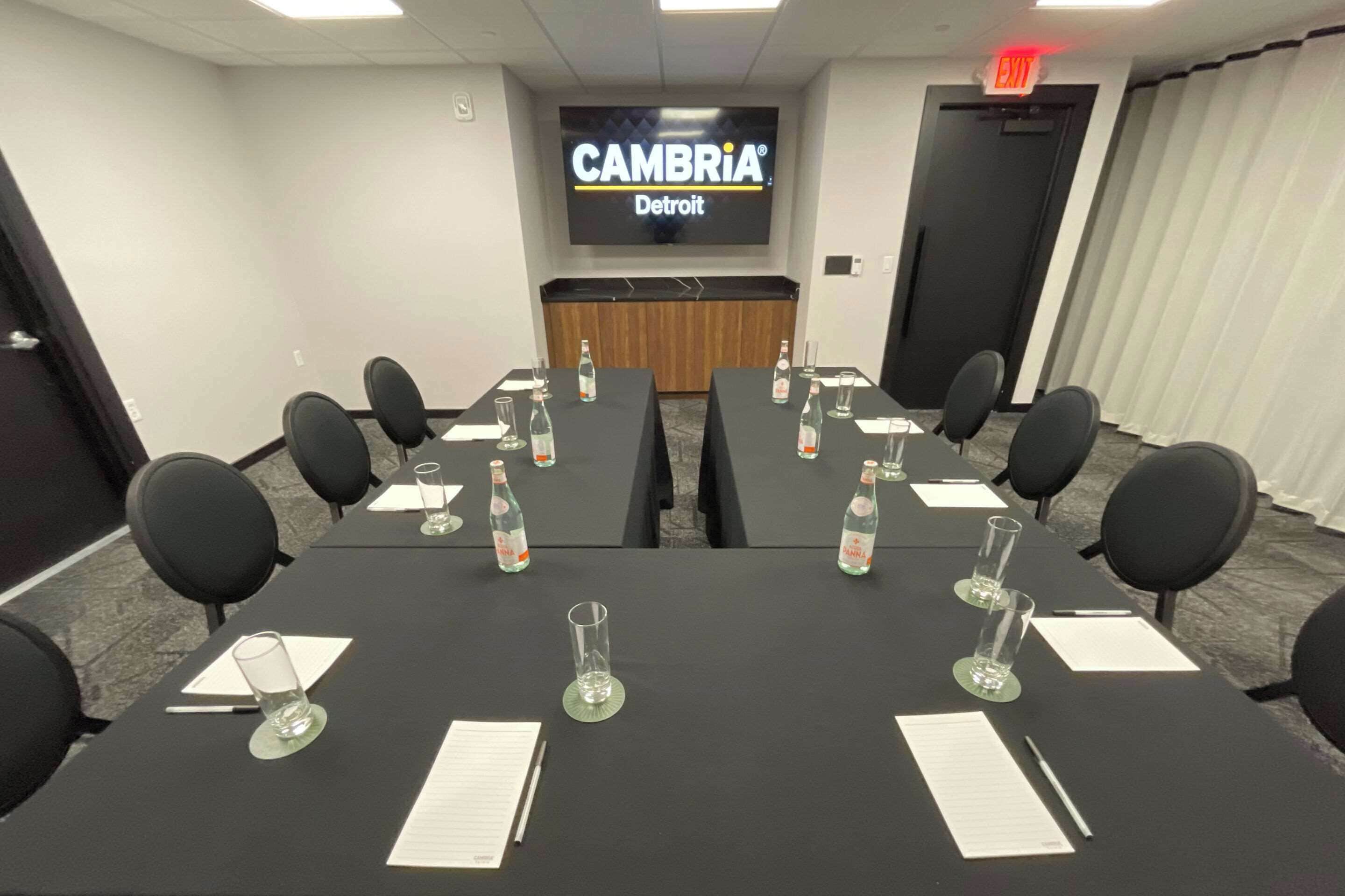 A conference room with a large screen displaying "CAMBRIA Detroit", tables with water bottles, and black chairs.