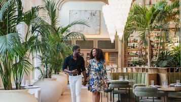 A spacious lobby with a high ceiling, large potted plants, and a bar area with shelves of bottles.