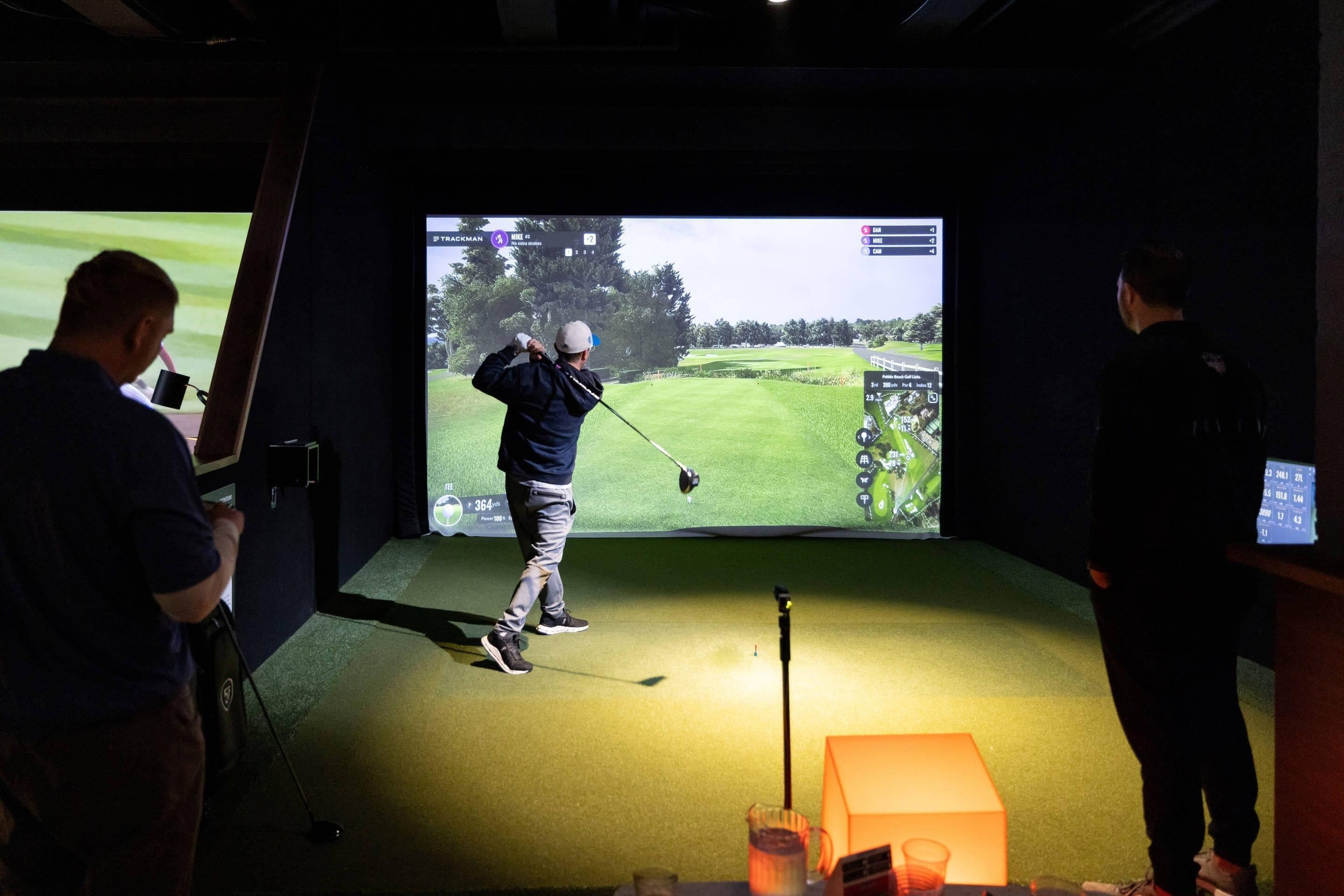 A golf simulation setup with a large screen, a golf club, and a target.