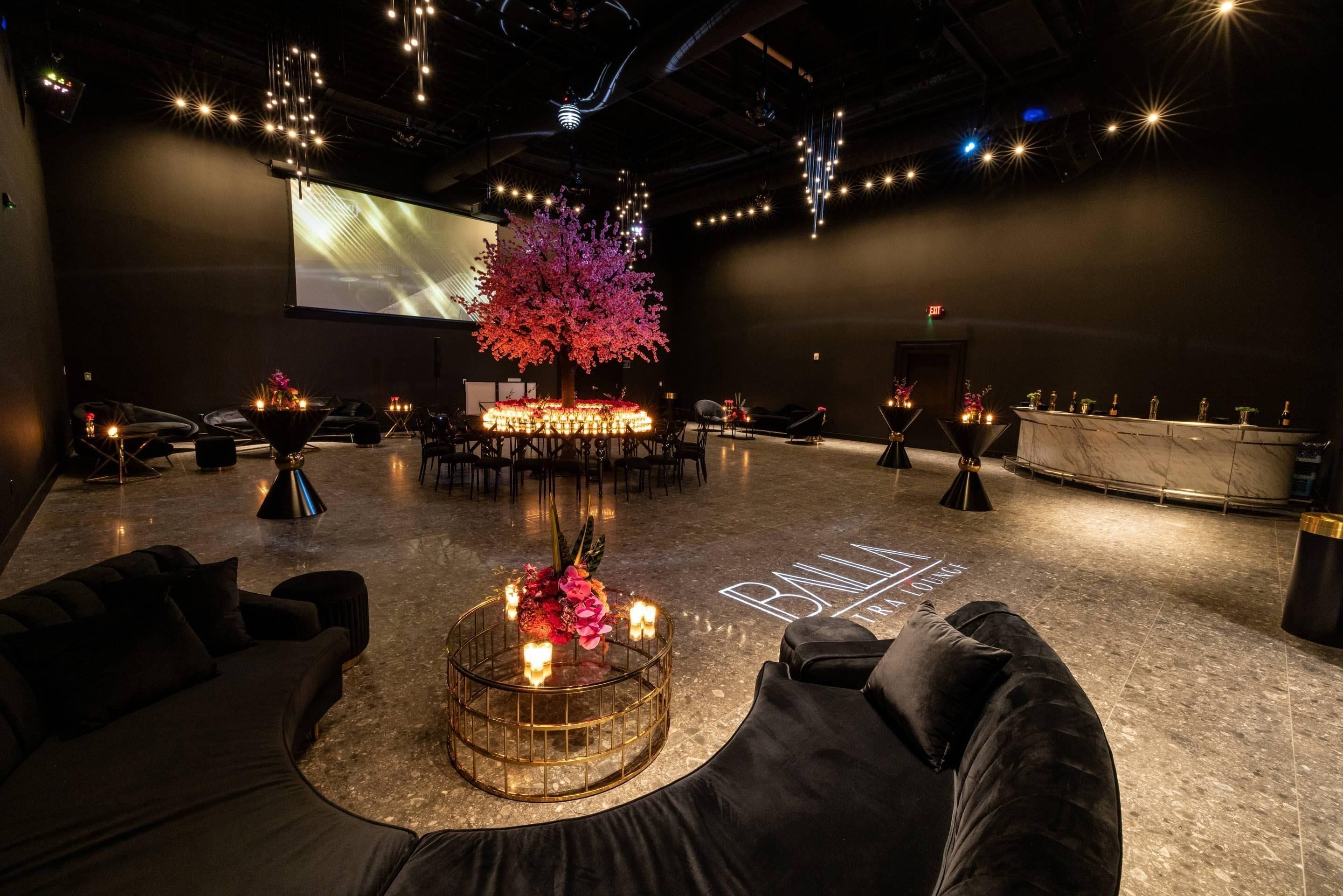 A modern lounge area with a central round table, seating arrangements, and a large screen.