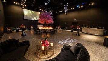 A modern lounge area with a central round table, seating arrangements, and a large screen.