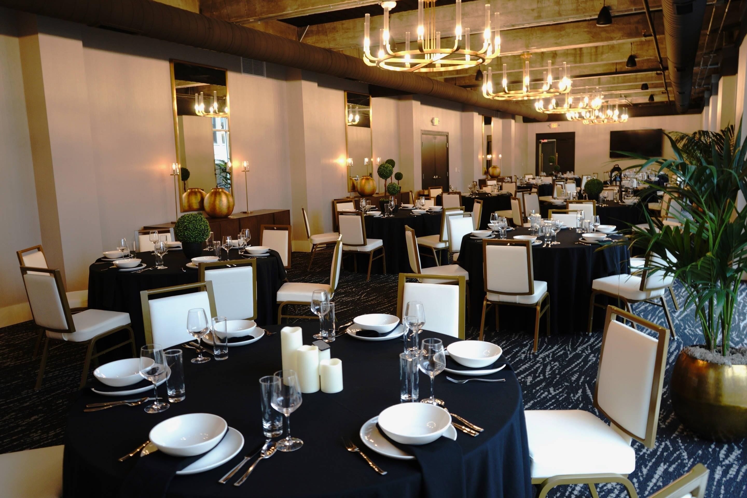 A banquet hall with multiple round tables set for dining, each with white plates, cutlery, and glasses.