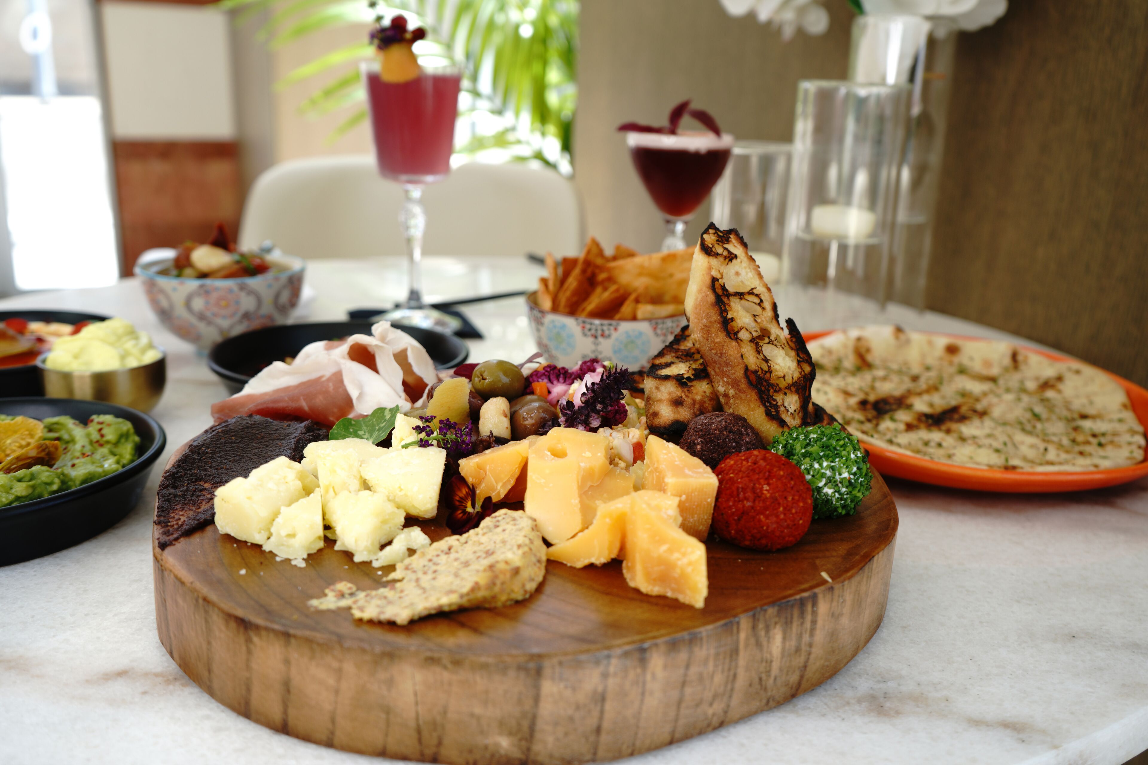A wooden board with various cheeses, fruits, and crackers.