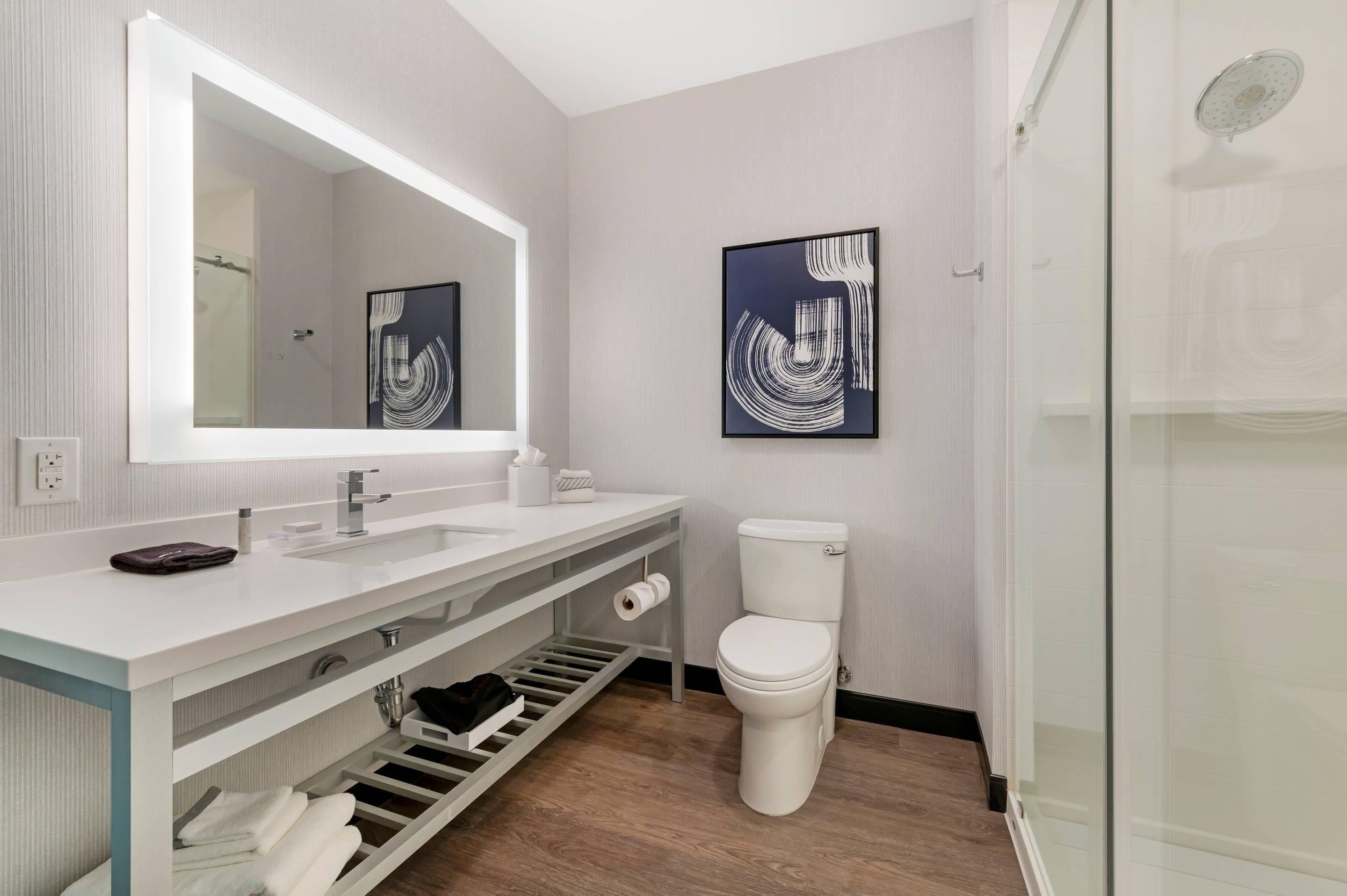 A modern bathroom with a large mirror, white fixtures, a toilet, and a glass shower enclosure.