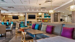 A modern restaurant with a bar area, seating arrangements, and a television screen. - Home2 Suites by Hilton Tucson Airport (Tucson)