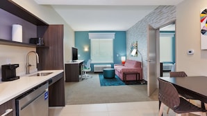 A modern kitchen with a dishwasher, a coffee maker, and a flat-screen TV. There is a dining area with a table and chairs, and a living room with a sofa and a coffee table. - Home2 Suites by Hilton Tucson Airport (Tucson)