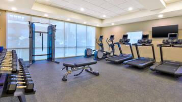 Une salle de sport équipée de tapis de course, de vélos elliptiques, d’un banc de musculation et d’haltères.
