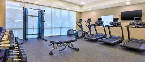 A gym with treadmills, elliptical machines, a weight bench, and dumbbells.
