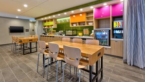 A modern restaurant with a wooden dining table and chairs, a kitchen area, and a colorful interior. - Home2 Suites by Hilton Tucson Airport (Tucson)