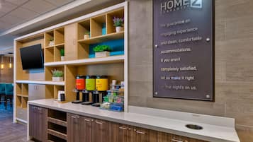 A reception area with a 'HOME2 GUARANTEE' sign, a coffee station, and a trash bin.