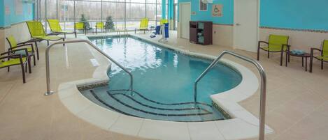 Una piscina interior con agua cristalina, rodeada de sillas de descanso y un elevador para piscina.