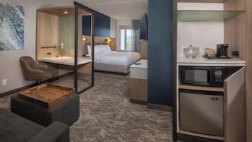 Quarto de hotel com cama, escrivaninha, cadeira, pequena cozinha e vista para o exterior.