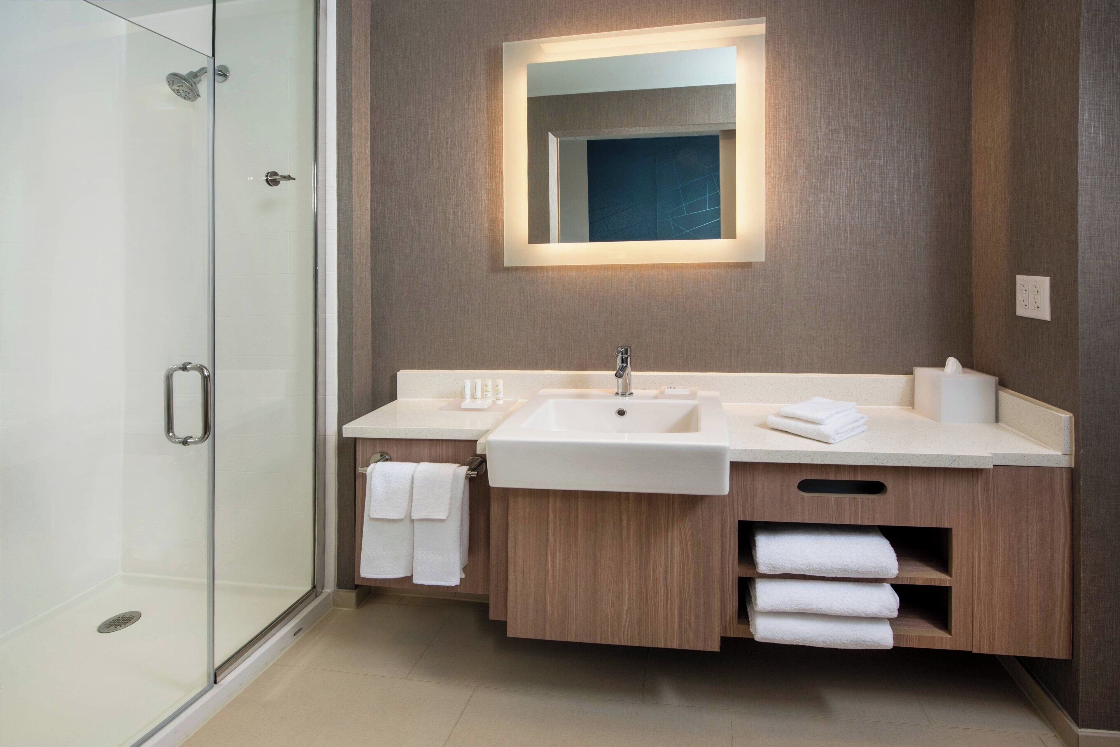 Un baño moderno con cabina de ducha de vidrio, un espejo grande y muebles de madera.