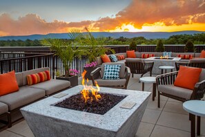 A rooftop terrace with outdoor seating, a fire pit, and a view of the sunset over a mountainous landscape. - SpringHill Suites by Marriott Frederick (Frederick)