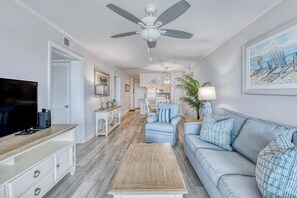 A living room with a television, sofa, coffee table, and ceiling fan.