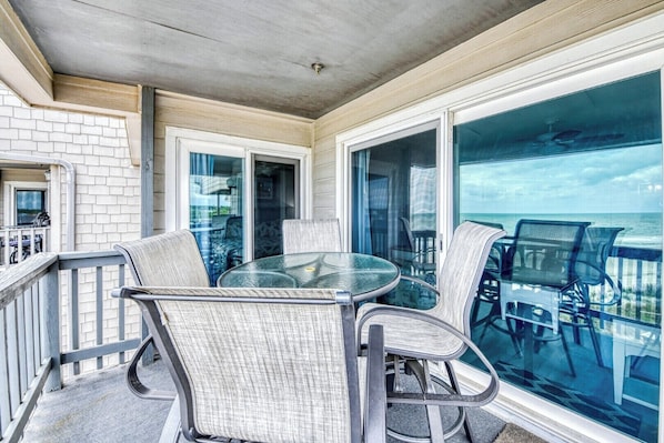 A balcony with a glass table and chairs, a view of the ocean, and a brick wall.