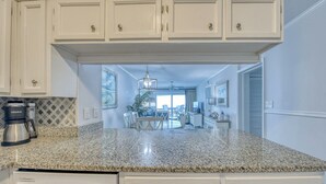Una cocina con encimeras de granito, muebles blancos y una cafetera Keurig.