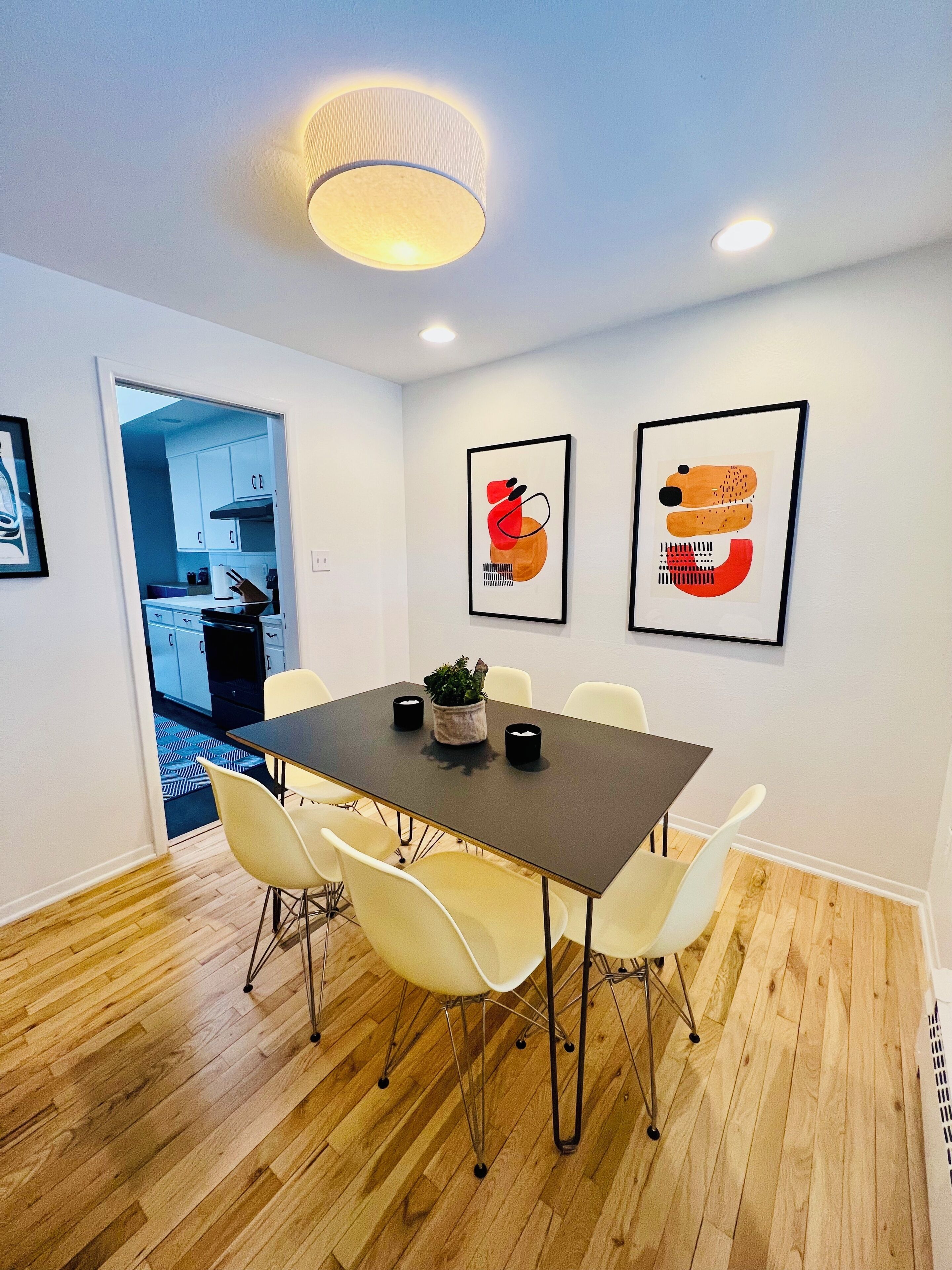 A modern dining area with a dark table, white chairs, and two framed abstract artworks on the wall.
