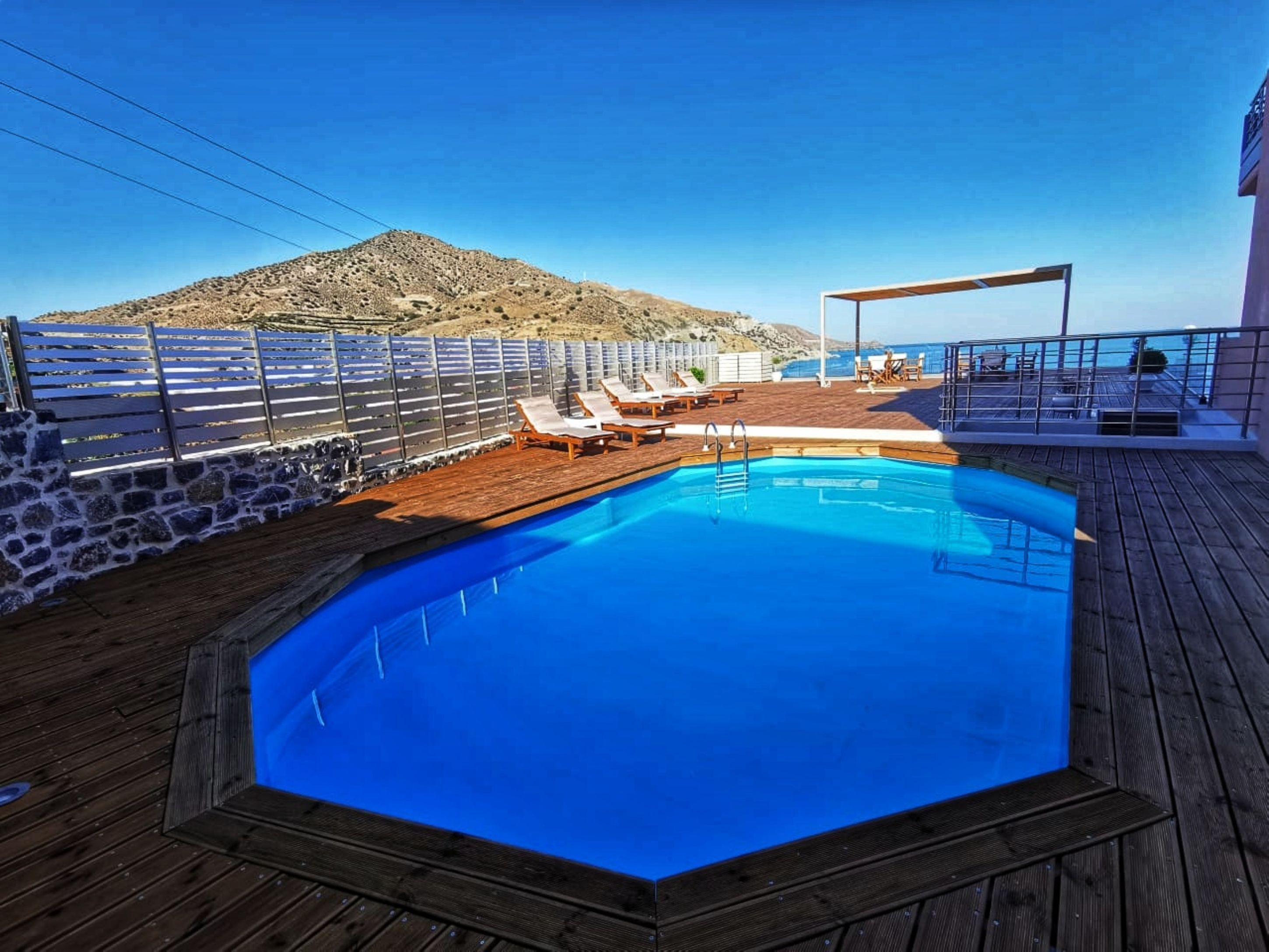 Ein Pool mit Holzterrasse, Liegestühlen und einer Steinmauer.