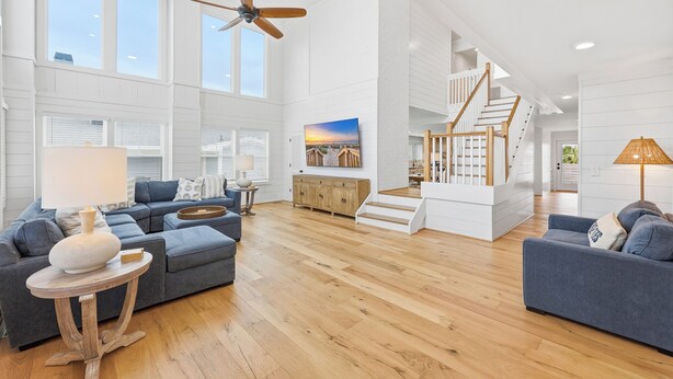 A spacious living area with a high ceiling, large windows, a wooden floor, a staircase, and a ceiling fan. - Cat Daddy 11 bedroom in North Litchfield, Pawleys Island (Pawleys Island)