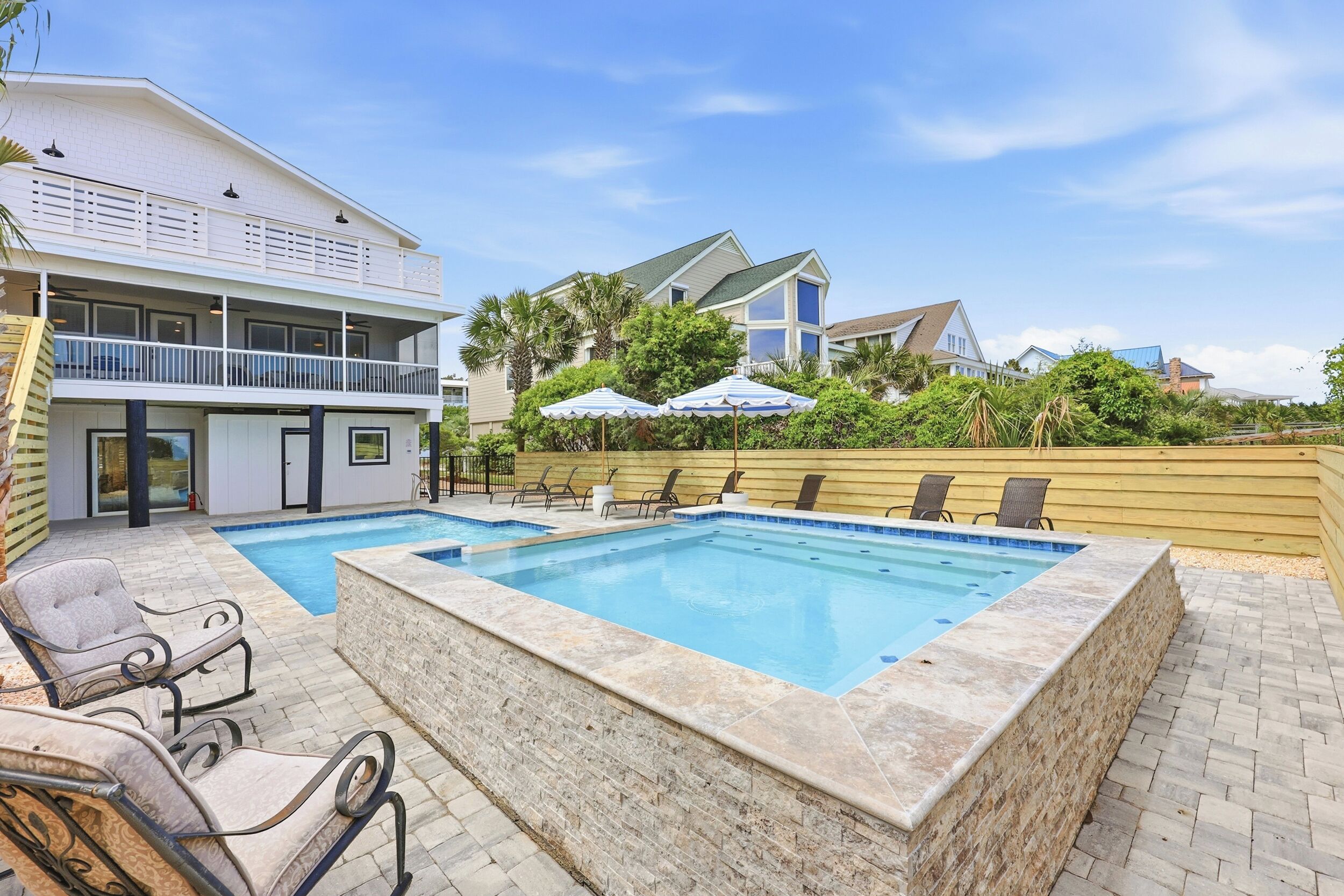 A swimming pool with lounge chairs, a covered seating area, and a multi-story building with balconies.