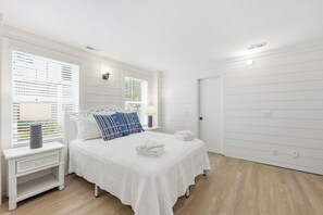 Un dormitorio con cama, mesitas de noche, una ventana con persianas y una puerta.