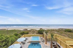 A pool area with a view of the beach, wooden deck, and lounge chairs.