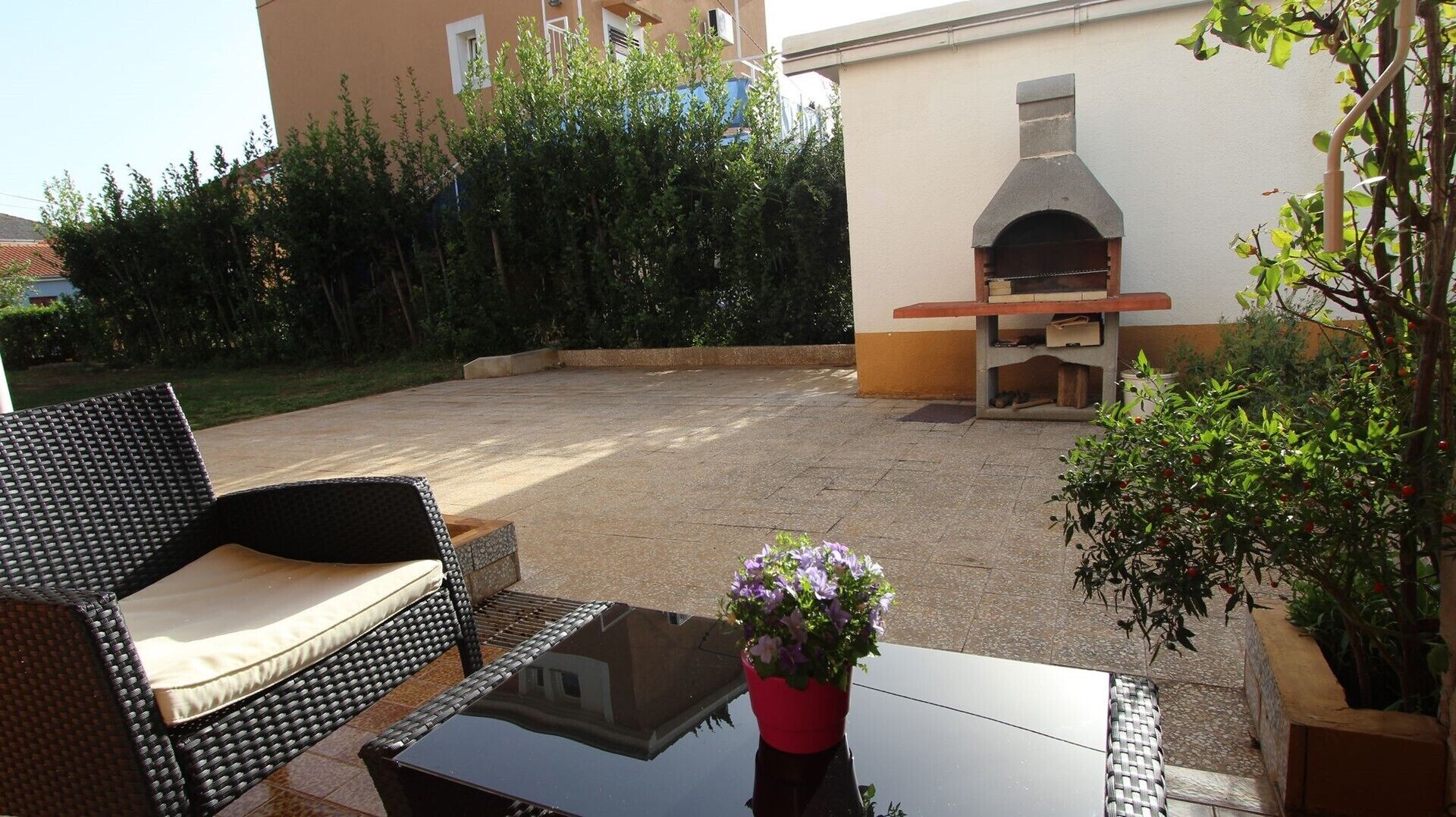An outdoor patio with wicker furniture, a glass table, and a potted plant.