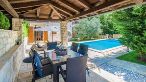 Un patio techado con mobiliario exterior, una piscina y un muro de piedra.
