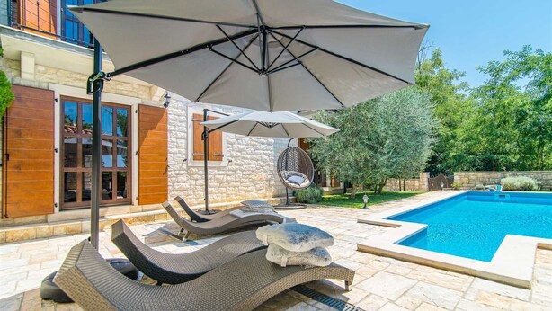 Zona junto a la piscina con un patio de piedra, una hamaca colgante y una sombrilla grande.