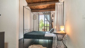 Un dormitorio con una cama, una mesita redonda con una lámpara, un manto de piel sintética y una ventana con cortinas.