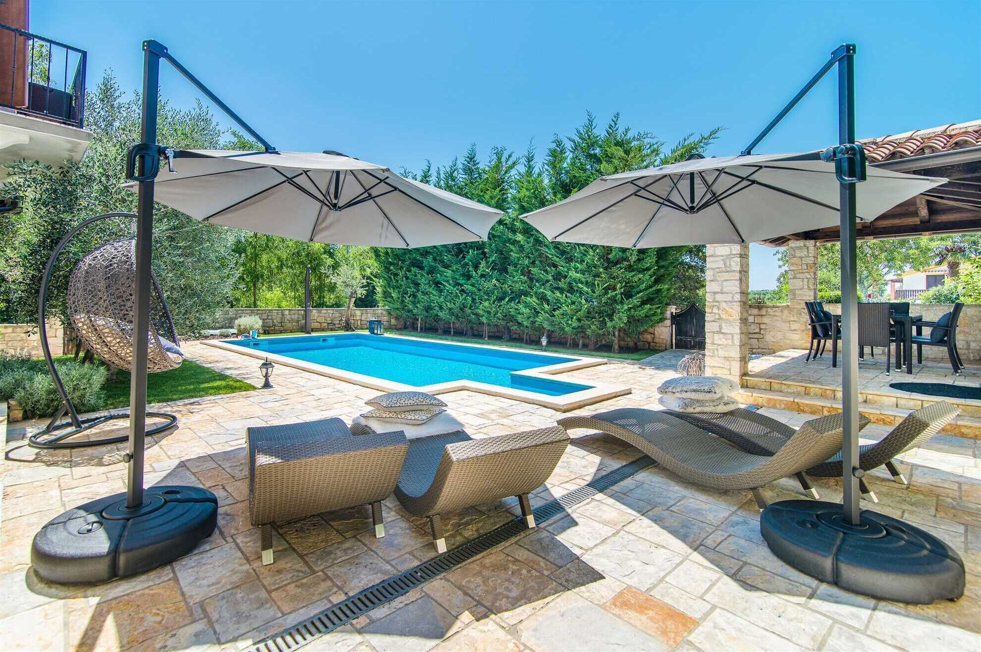 Een zwembadgedeelte met buitenmeubilair, parasols en een terras van natuursteen.