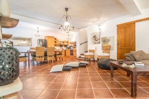Amplia sala de estar con una mesa de comedor, sillas de mimbre, un sofá y una cocina al fondo.