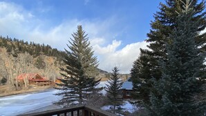 Un pont de fusta amb escales cobertes de neu que condueixen a una vista d'un llac gelat, envoltat d'arbres de fulla perenne i un edifici allunyat amb teulada vermella.