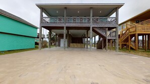 A building with a covered entrance, wooden deck, and a staircase leading to a balcony. - Ocean Jewel: 3  BR, 2  BA House in Port Bolivar, Sleeps 10 (Bolivar Peninsula)