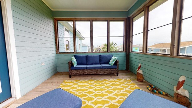 A room with a blue sofa, a yellow patterned rug, and large windows. - Ocean Jewel: 3  BR, 2  BA House in Port Bolivar, Sleeps 10 (Bolivar Peninsula)