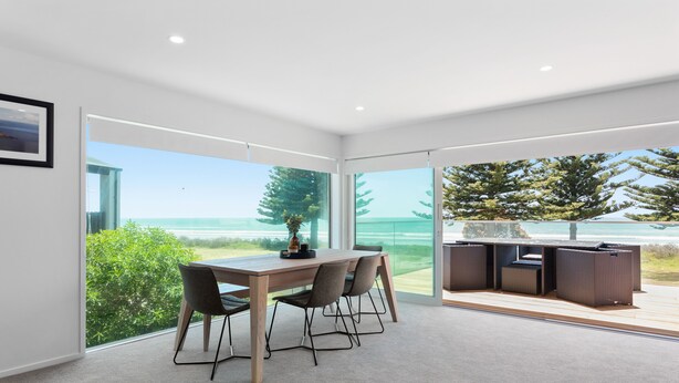A modern interior with a dining area, large windows, and a view of the sea.
