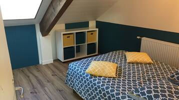 A bedroom with a sloped ceiling, a bed with patterned bedding, two pillows, a storage unit, and a radiator.